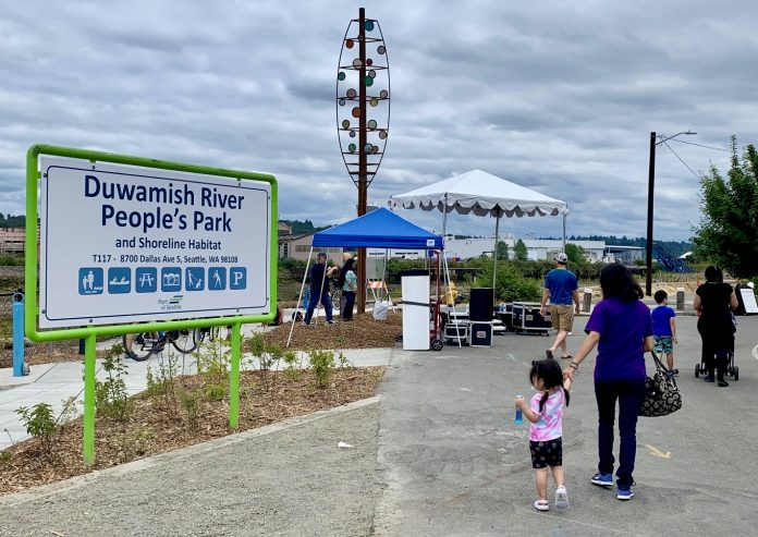 a sign for duwamish people's park with a woman and young child walking by