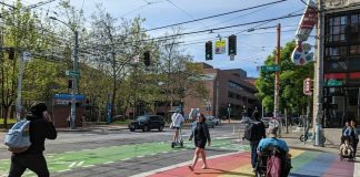 people walk and roll across a rainbow painted crosswalk