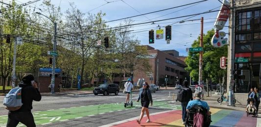 people walk and roll across a rainbow painted crosswalk