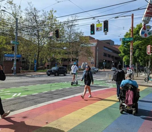 The Seattle Transportation Plan Must Be Bold people walk and roll across a rainbow painted crosswalk