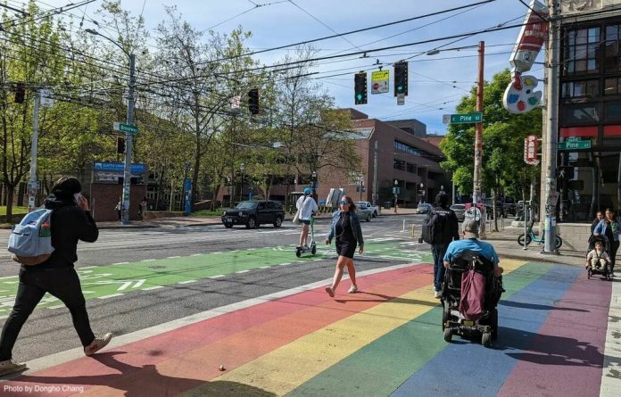 people walk and roll across a rainbow painted crosswalk