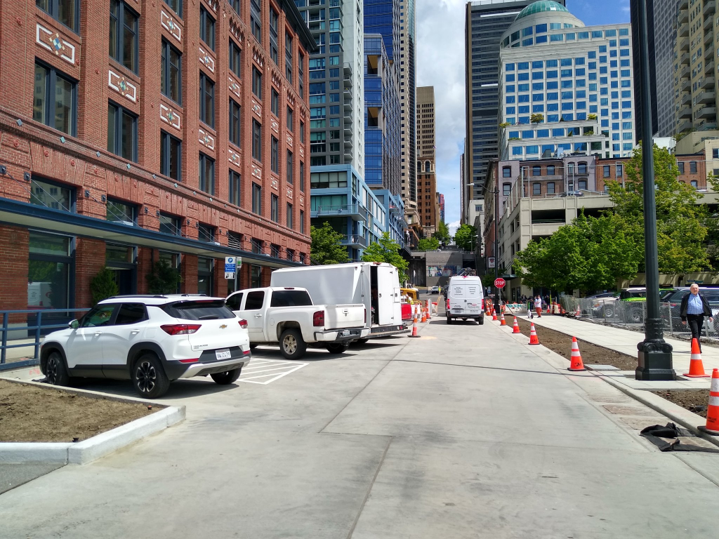 Photograph of a street with back angle parking, a one way travel lane and a fairly wide sidewalk on one side