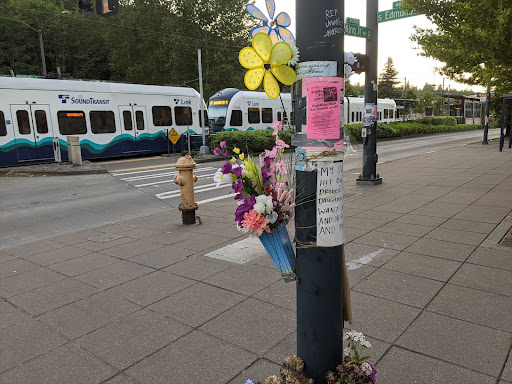 The photo is of a heartbreaking memorial of flowers and floral pinwheels left on a light pole by Jennette’s loved ones near where she lost her life. A light rail train is in the background. The sign that’s part of the memorial says “My sister Jennette was hit by 2 cars on June 6. One driver hit and ran. She was a daughter, aunt and mother. We want justice for our family and her son. Forever loved and missed.