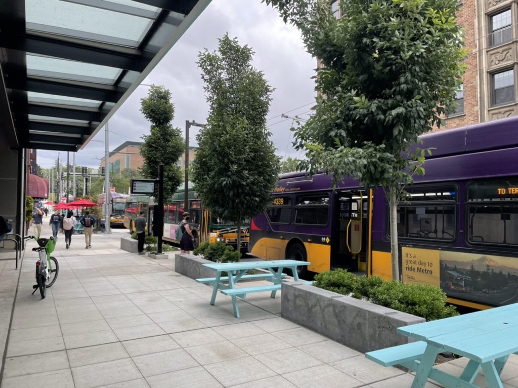 Pedestrians walk along the sidewalk and wait for buses.