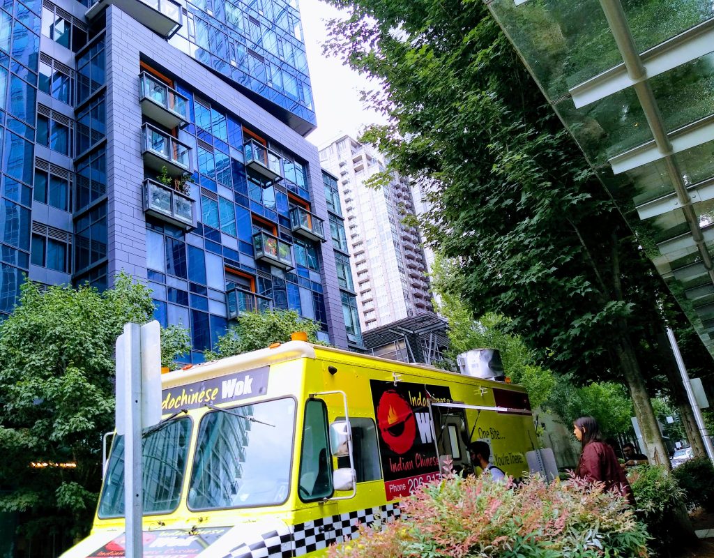 A photo of food truck on a street with tall buildings.