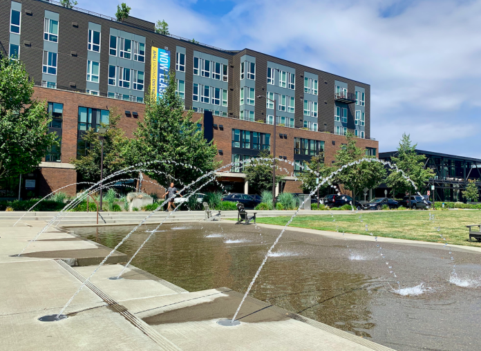 A photo of a fountain with an apartment building behind it.