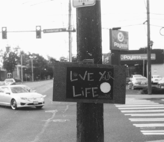 The View From Nathan’s Bus: Doin’ You Black and white photo of a large surface intersection and turning car with a telephone pole right in the middle bearing a sign saying "Live Your Life"
