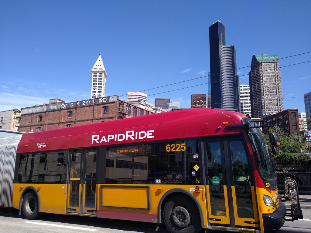 A red and gold RapidRide bus in Pioneer Square with the Seattle skyline in the background.