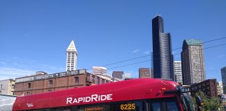 A red and gold RapidRide bus in Pioneer Square with the Seattle skyline in the background.