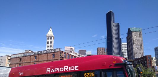 A red and gold RapidRide bus in Pioneer Square with the Seattle skyline in the background.
