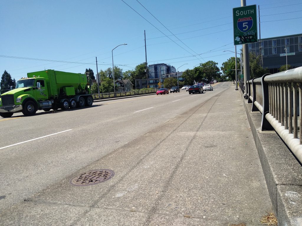 An I-5 overpass with traffic on it and an I-5 South sign on it, some buildings in the distance