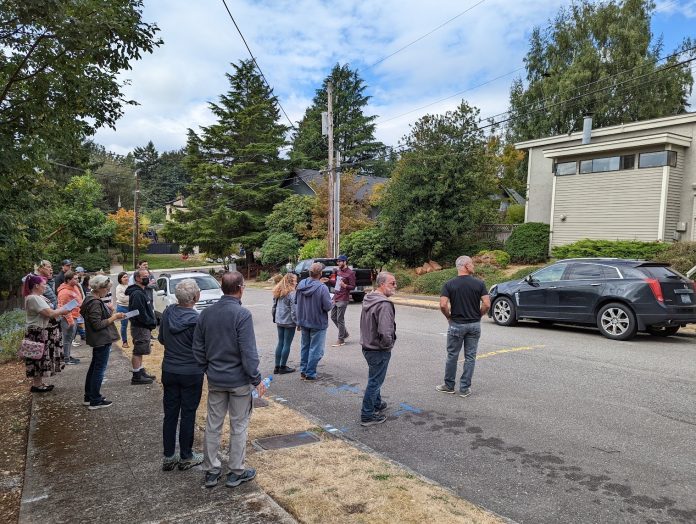 A photo of a group of people standing in the street in front of a small multi-family home.