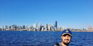 Rian Watt, pictured here with Elliott Bay and the Seattle Skyline. He wears a Mariners hat.