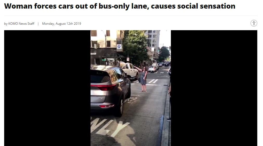 The KOMO News caption read "Woman forces car out of bus only lane, causes social sensation." A woman in a dress and sunglasses stands in the bus only lane and funneled scofflaw motorists out of it.