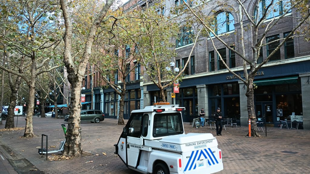 A small 3 wheeled parking enforcement sits on a pedestrian street with an officer strolling toward it