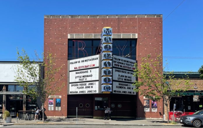 Street scape brick facade movie theater building in front of a blue sky featuring a marquee advertising Majestic Bay, Guardians 3, Little Mermaid, Fast X and coming attractions of Indiana Jones and Spiderverse.