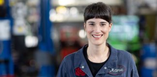 A young dark-haired woman in her blue autobody shop overalls.