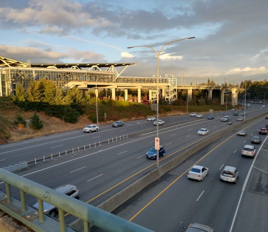 Tukwila Gets Serious about Transit-Oriented Housing The elevated station gleams as the sun is going down over a busy freeway trench.