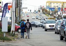 Seattle Greenways Offers Their Own 90-Day Review of SDOT’s Vision Zero Safe Streets Campaign Rows of cars on a block of drive thrus and strip malls as two kids walk in the gutter of the road.