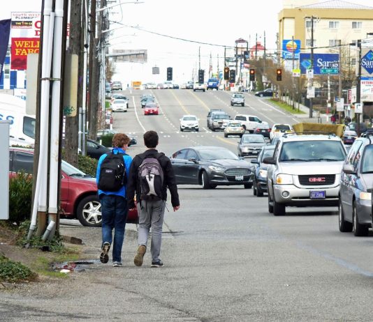 Aurora Avenue Community Workshops Kick Off in June Rows of cars on a block of drive thrus and strip malls as two kids walk in the gutter of the road.