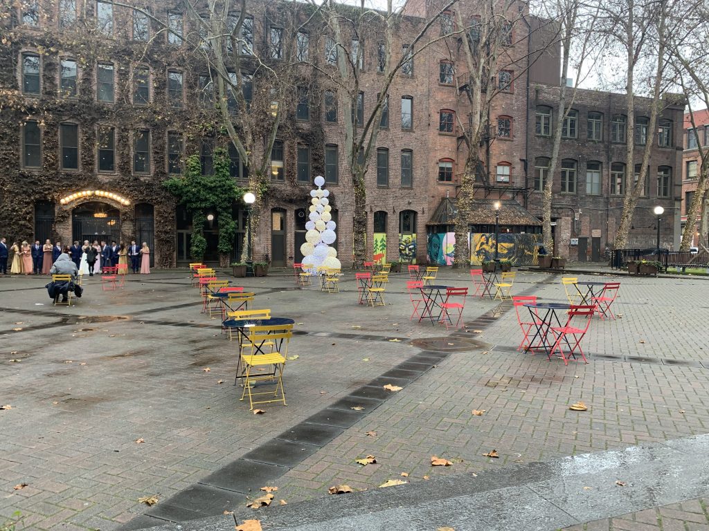 A plaza with Christmas lights and many empty tables. 