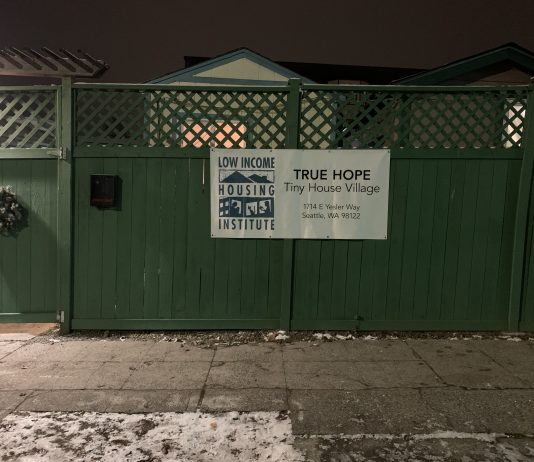 Tiny House Villages Take on Freezing Temperatures A sign for True Hope Tiny House Village on a green fence in front of a snowy sidewalk.