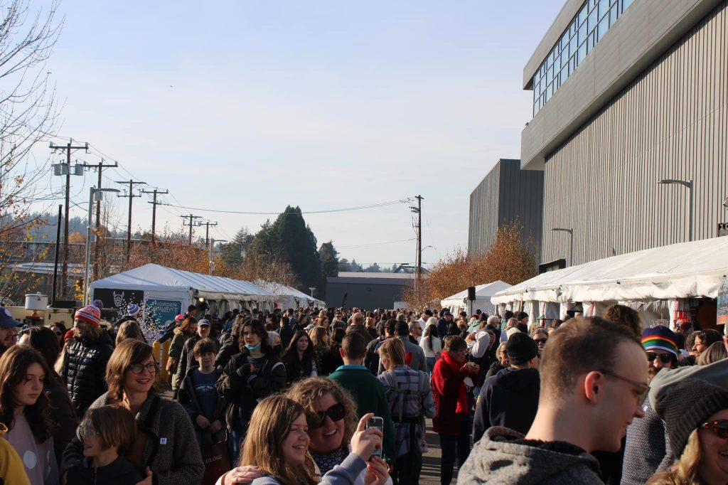 People crowded between white tents in the middle of the day. 