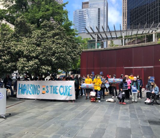 Housing Coalition Passes Tenant Protections Across King County A Stay Housed rally with a "Housing is the Cure" banner at Seattle City Hall with a crowd of about 50.
