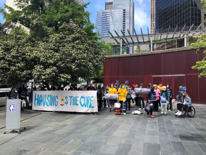 Stay Housed rally at Seattle City Hall via Stay Housed Coalition A Stay Housed rally with a "Housing is the Cure" banner at Seattle City Hall with a crowd of about 50.
