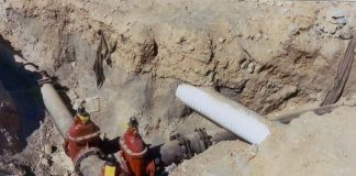 Trench cut in dirt with an intersection of iron pipes and a lightly colored stormwater crossing.