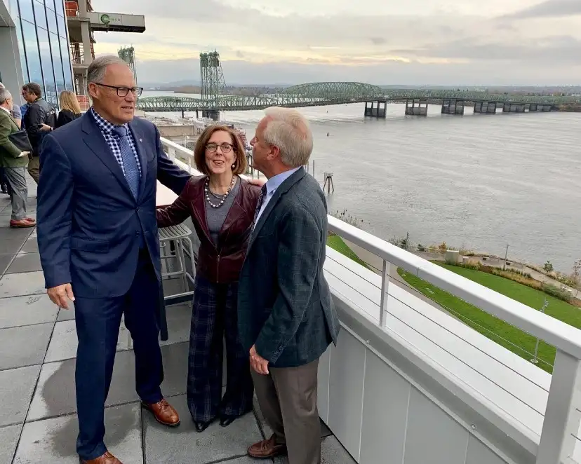 Governor Inslee and Brown on a balcony with their arms around each other with the current I-5 bridge in the background