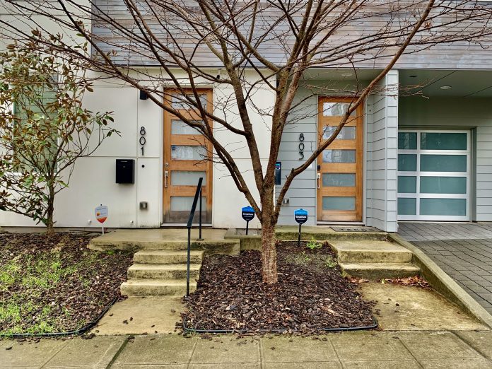 two doors with addresses with a tree in the center and drive with garage in back