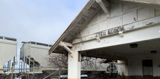 A photo of the abandoned Steilacoom Rail Depot with a freight train behind it.