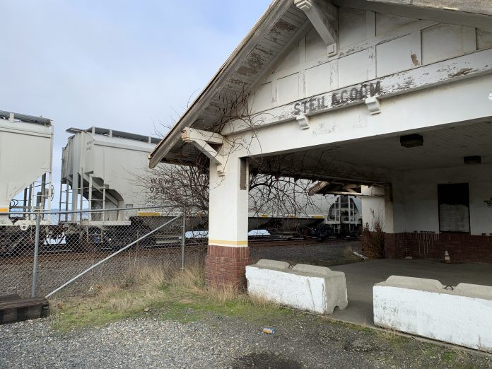 A photo of the abandoned Steilacoom Rail Depot with a freight train behind it.
