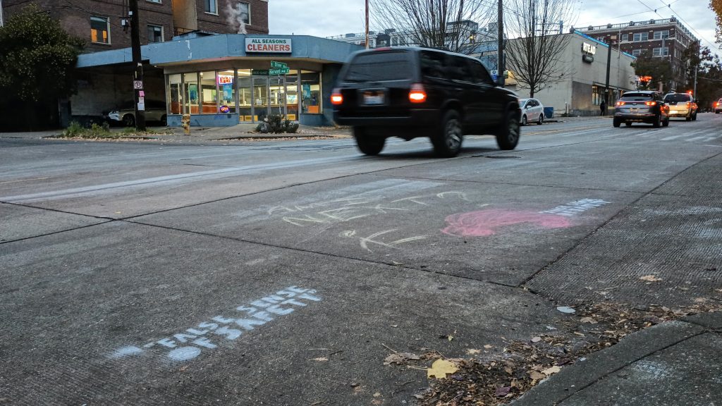 An unmarked crosswalk with chalk writings including "false sense of safety" on the concrete street
