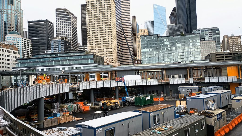 A curving walkway leads to the new entry building under construction with the rest of downtown looming over the terminal