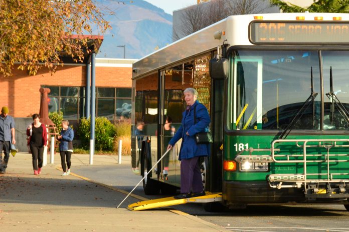 A green bus marked Route 305 Sedro Woolley with its ramp out to let a woman with a cane exit.