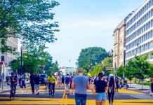 Report Ranking US Metros Shows Walkable Urbanism Pays Dividends People walk and bike on a wide street painted with yellow lines.