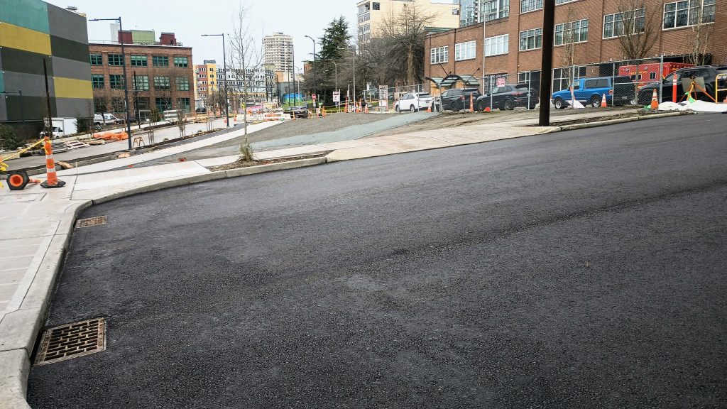 A new asphalt street with a triangle sized gravel pit where an EV charging lot was planned