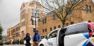 White van with passenger door open waits for riders in front of a brick building.