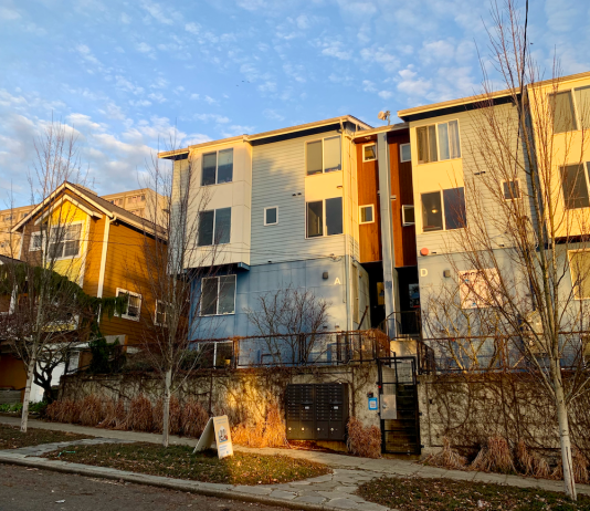 Seattle Proposes Co-Living Ordinance Seeking to Meet New State Mandate Microhousing building next to a single family home. Blue sky overhead and sunset lighting.