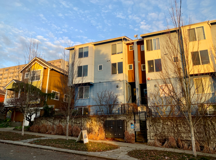 Microhousing building next to a single family home. Blue sky overhead and sunset lighting.