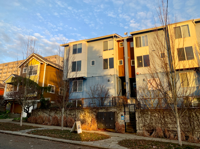 Microhousing building next to a single family home. Blue sky overhead and sunset lighting.