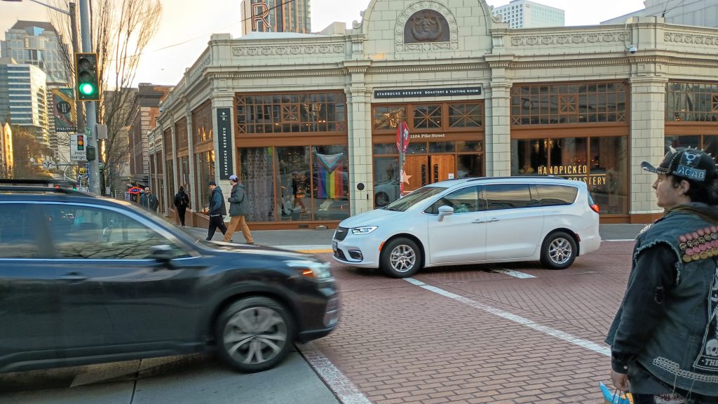 A confused pedestrian watches as drivers dominate a brick crosswalk