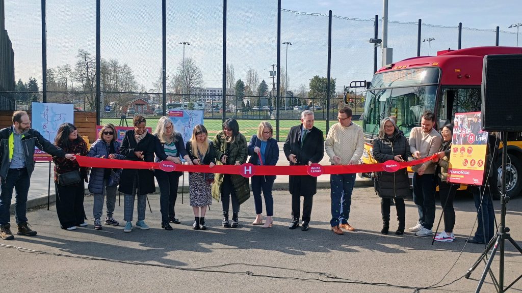 Officials cutting a ribbon in front of a RapidRide H bus
