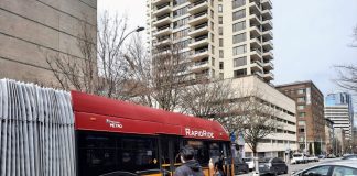 Two pedestrians and a car watch the RapidRide H bus go by.