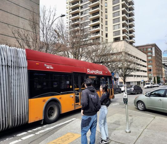 Bus Service Needs Investment Rather Than Neglect Two pedestrians and a car watch the RapidRide H bus go by.