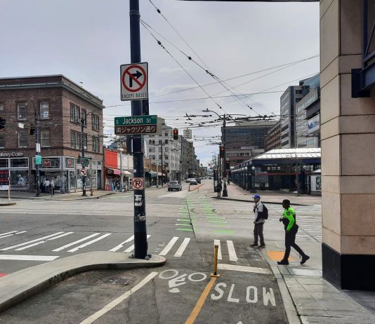 Sound Transit is Not Ready for Its Big Chinatown Station Decision Jackson Street with two pedestrians crossing at 5th Avenue next to the protected bike lane. The Chinatown station is in the background.