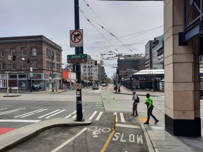 Jackson Street with two pedestrians crossing at 5th Avenue next to the protected bike lane. The Chinatown station is in the background.