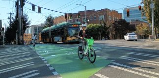 Someone riding a lime bike across a bike lane in Capitol Hill with a bus behind them